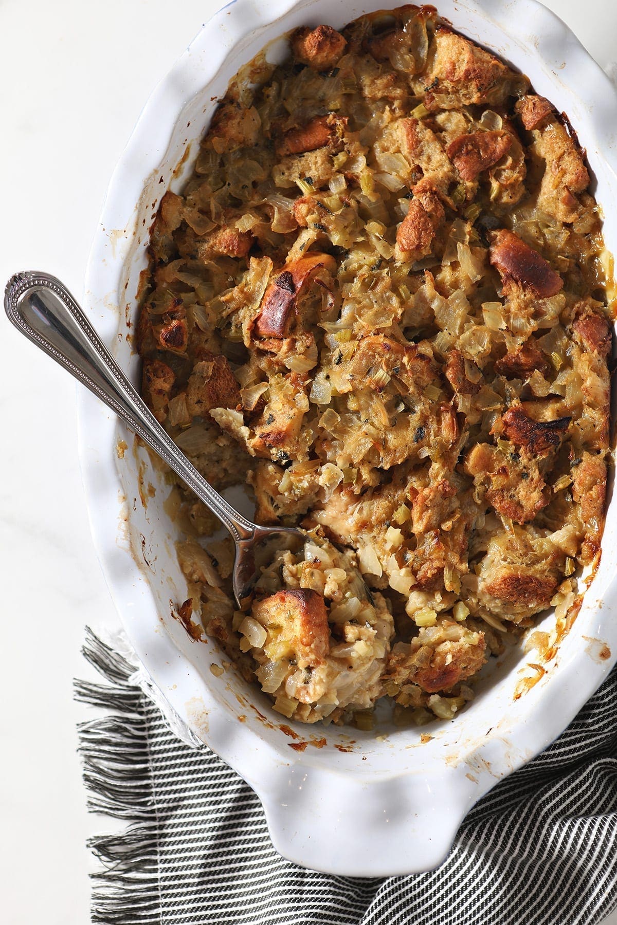 A spoon holding stuffing sits in a casserole dish holding the final baked dish