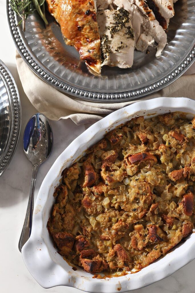 Brioche Bread stuffing in a casserole dish on the holiday table next to sliced turkey