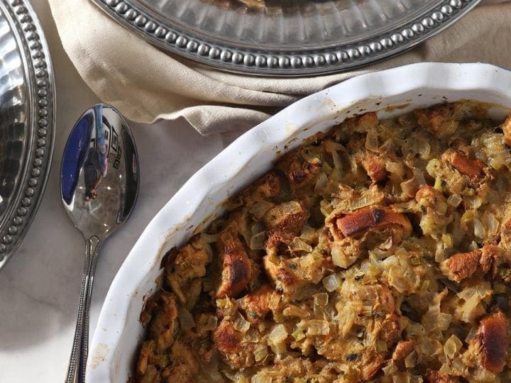 Brioche Bread stuffing in a casserole dish on the holiday table next to sliced turkey