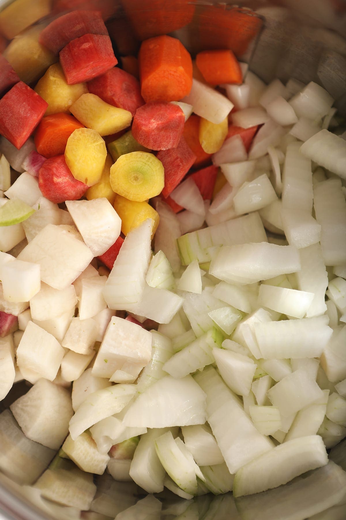 Close up of chopped onions, carrots and parsnips in a slow cooker