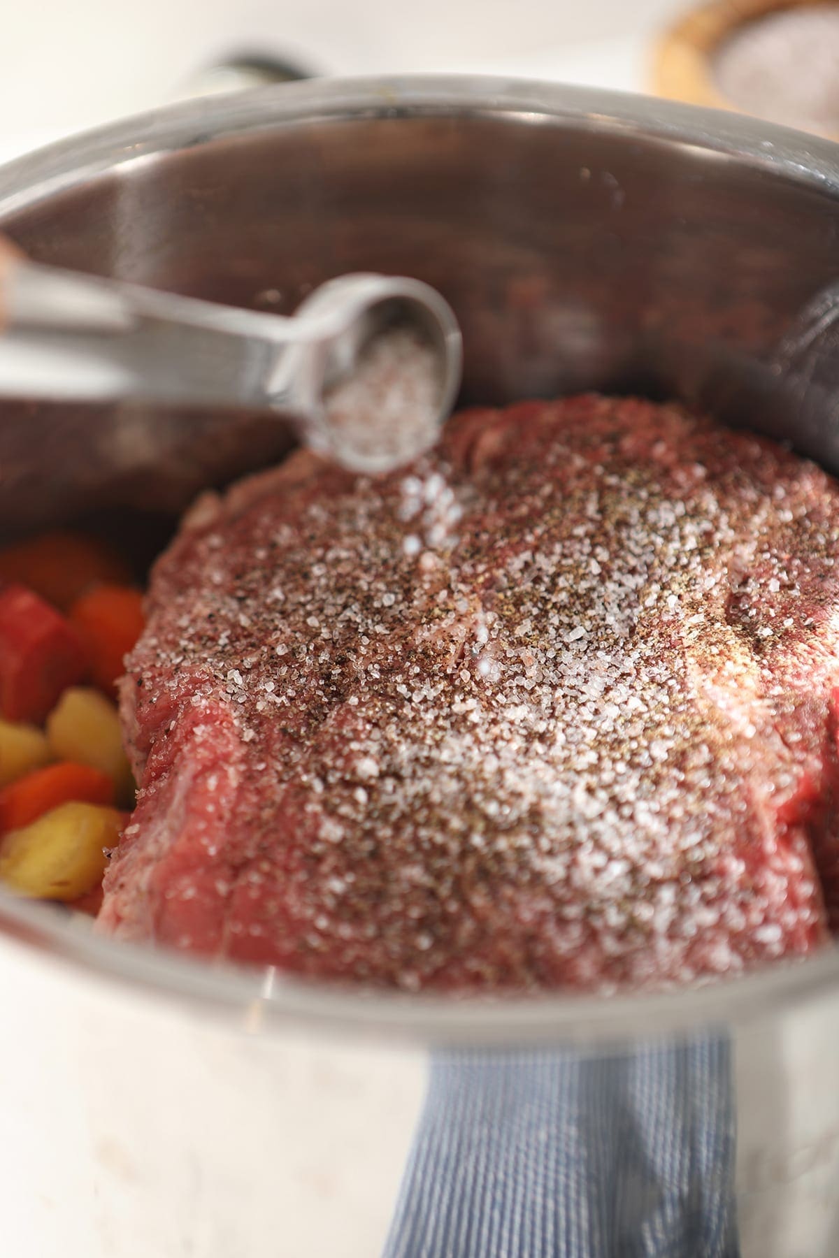 Seasonings are sprinkled on top of a beef roast in a slow cooker