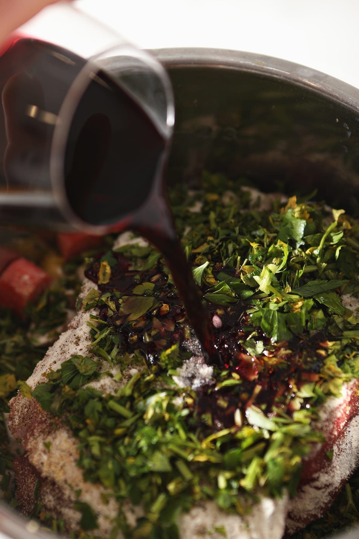 Red wine is poured into the basin of a slow cooker on top of a seasoned roast