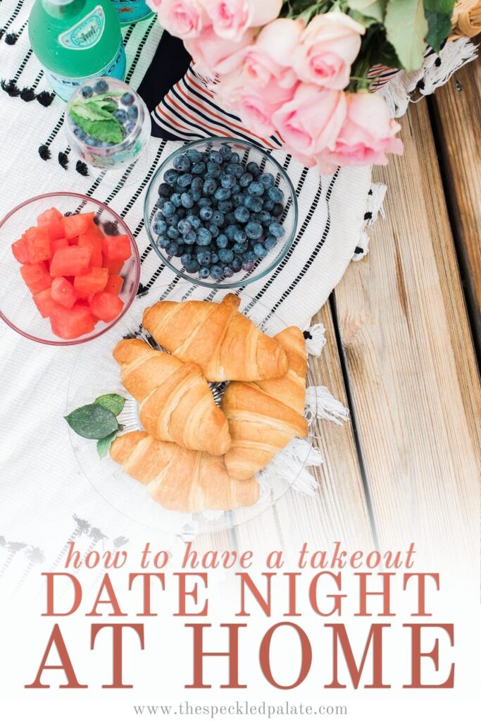 Overhead of a picnic spread with croissants, fruit and roses with the text 'how to have a takeout date night at home'