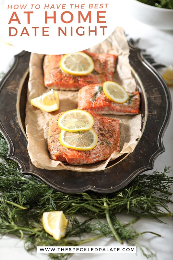 Close up of roasted salmon filets with lemon slices and thyme on them on a tarnished silver platter with the text 'how to have the best at-home date night'