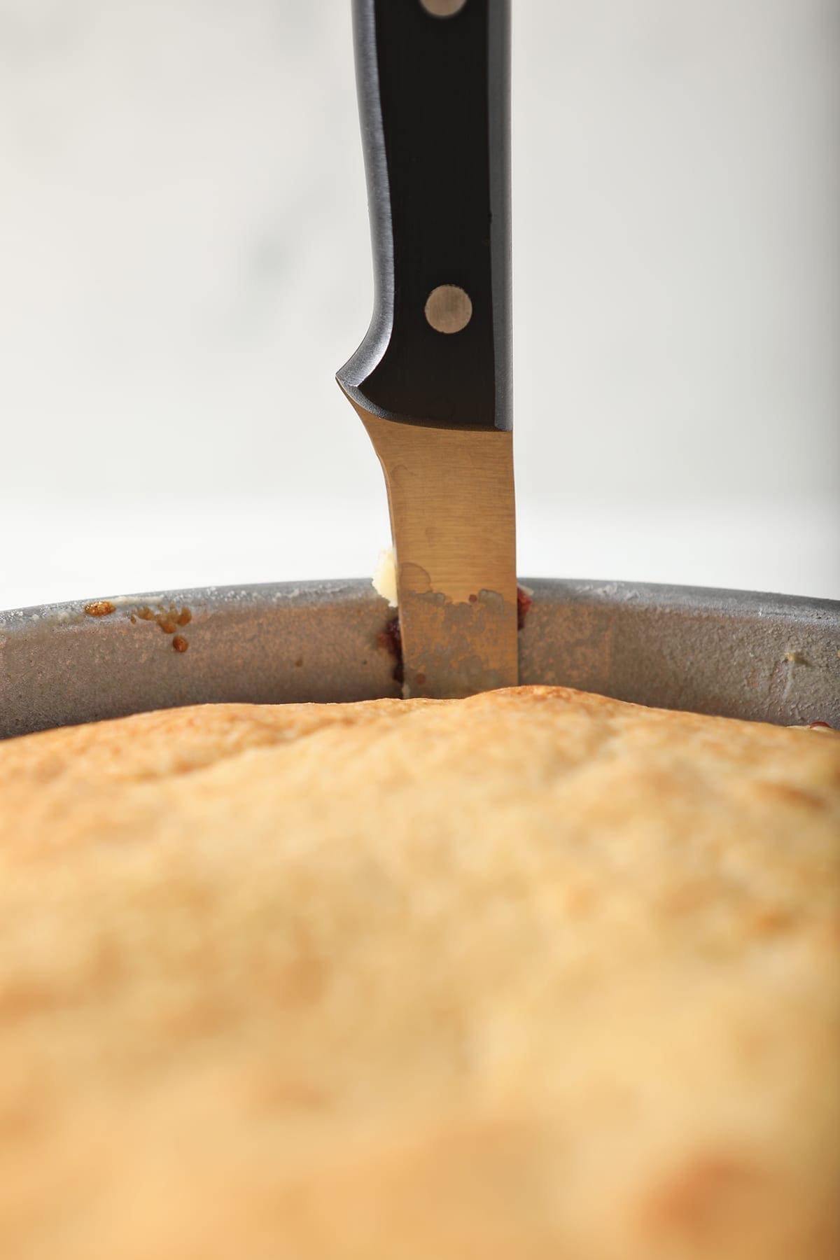 A paring knife runs along the side of a cake tin after the cake has cooled slightly