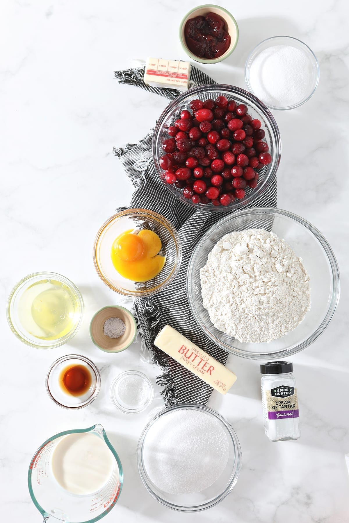 Ingredients for the Cranberry Cake, shown from above in bowls, on a gray striped towel and marble counter