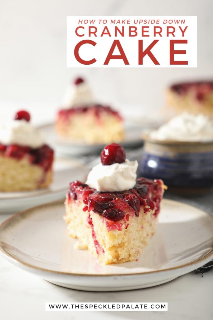 A slice of cranberry upside down cake garnished with a dollop of whipped cream and a cranberry on a white pottery plate with other slices behind it with the text 'how to make upside down cranberry cake'