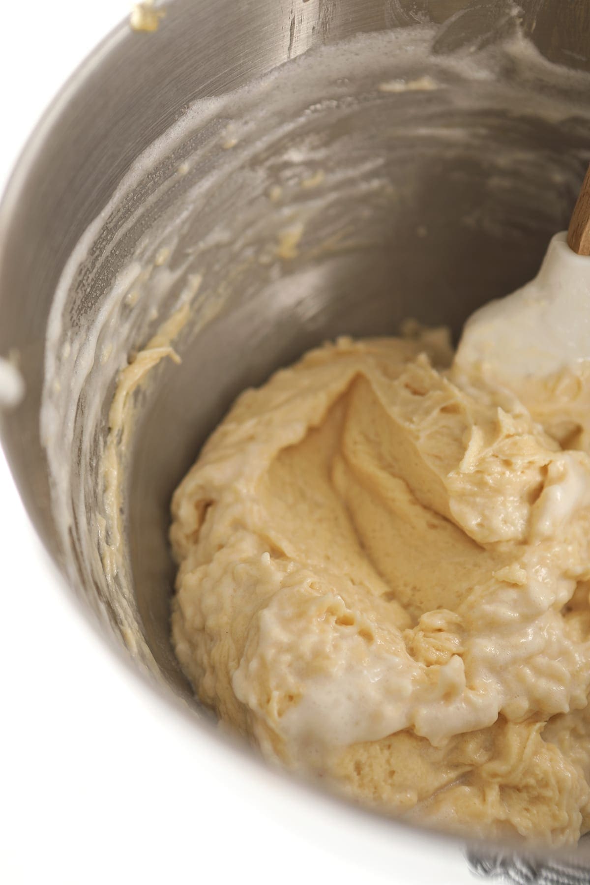 A white spatula stirs fluffy egg whites into cake batter