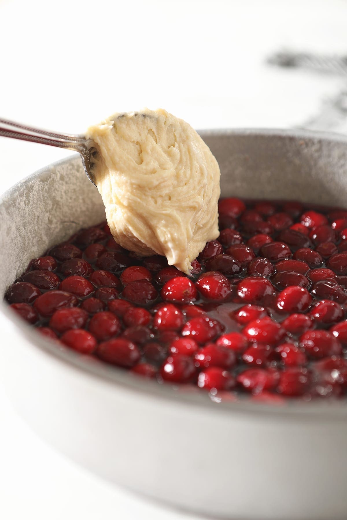 A spoon dollops cake batter on top of cranberries and their sauce