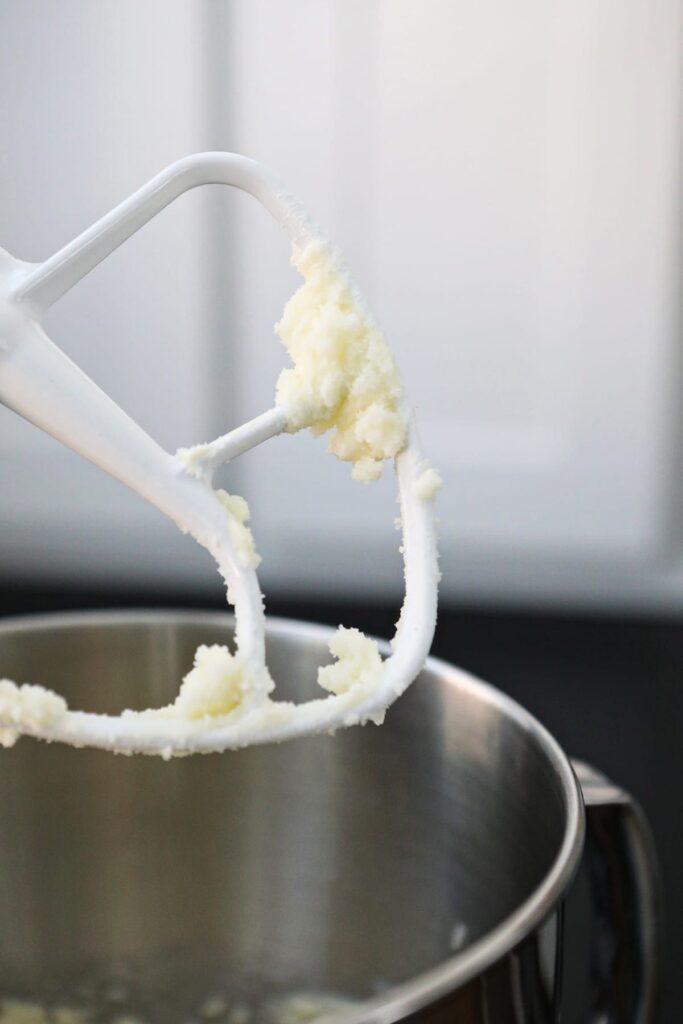 A stand mixer cookie paddle holds combined sugar and butter