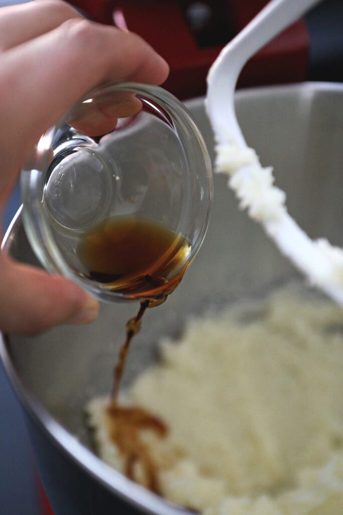 Vanilla extract is poured into a butter-sugar mixture in the stand mixer