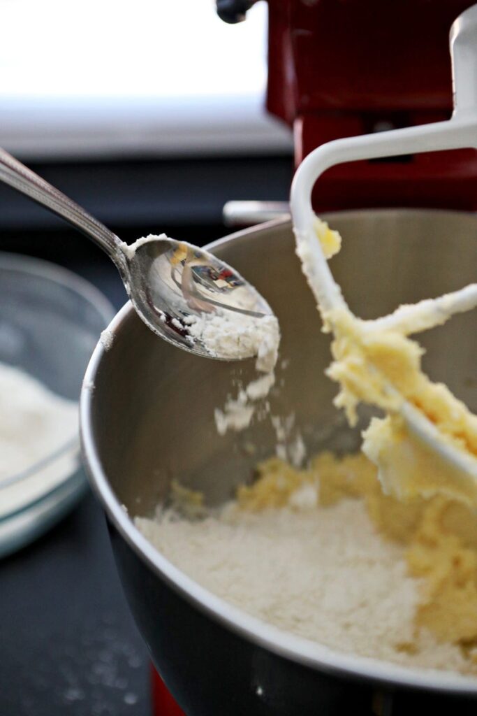 A spoon sprinkles flour into a stand mixer bowl