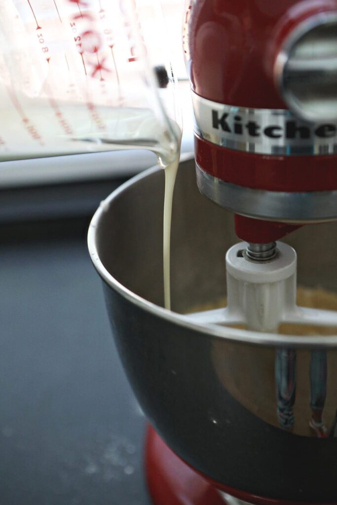 Cream is poured into a running stand mixer from a liquid measuring cup