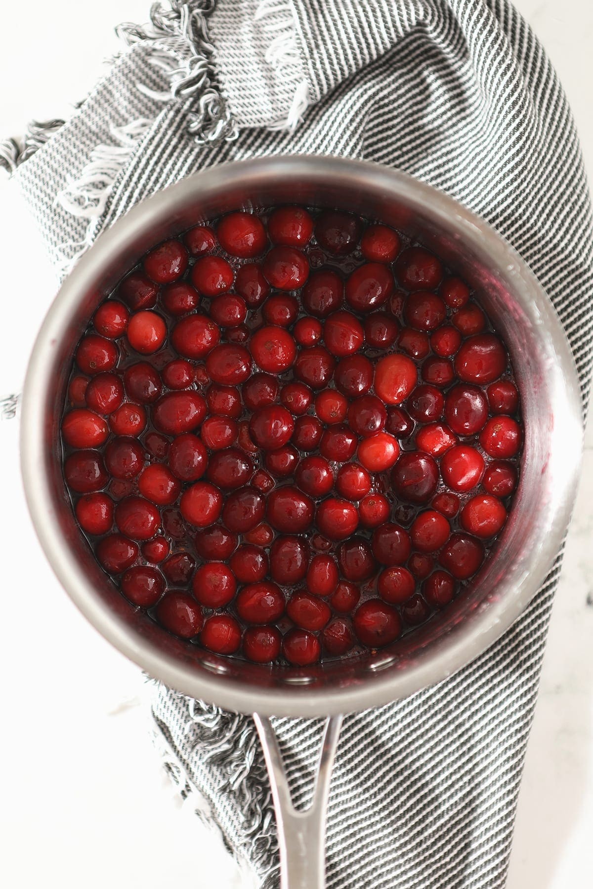 The cranberry sauce for the cake in a saucepan before draining on a gray towel