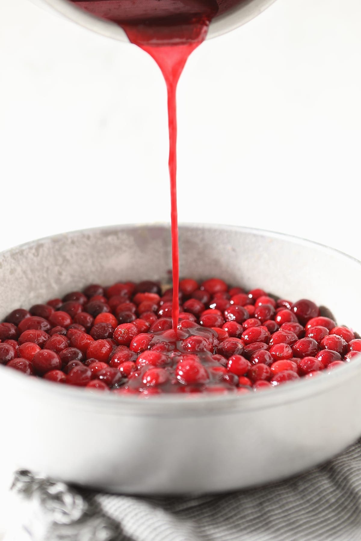 Sauce is poured on top of cranberries in a round cake pan