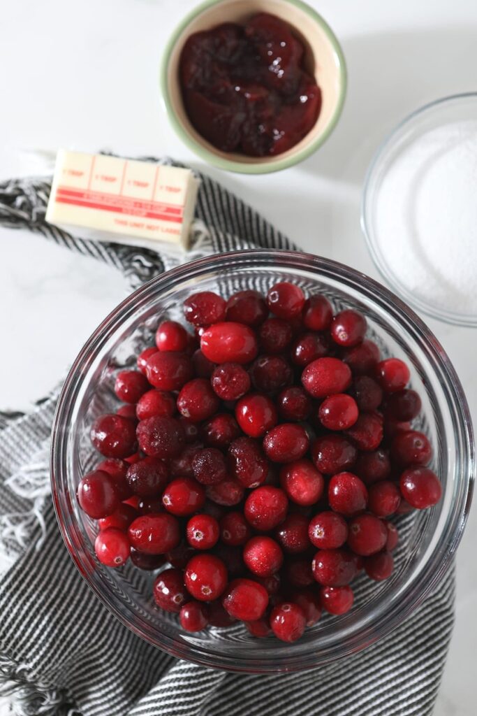 Cranberries in a bowl with jam, butter and sugar beside it on marble