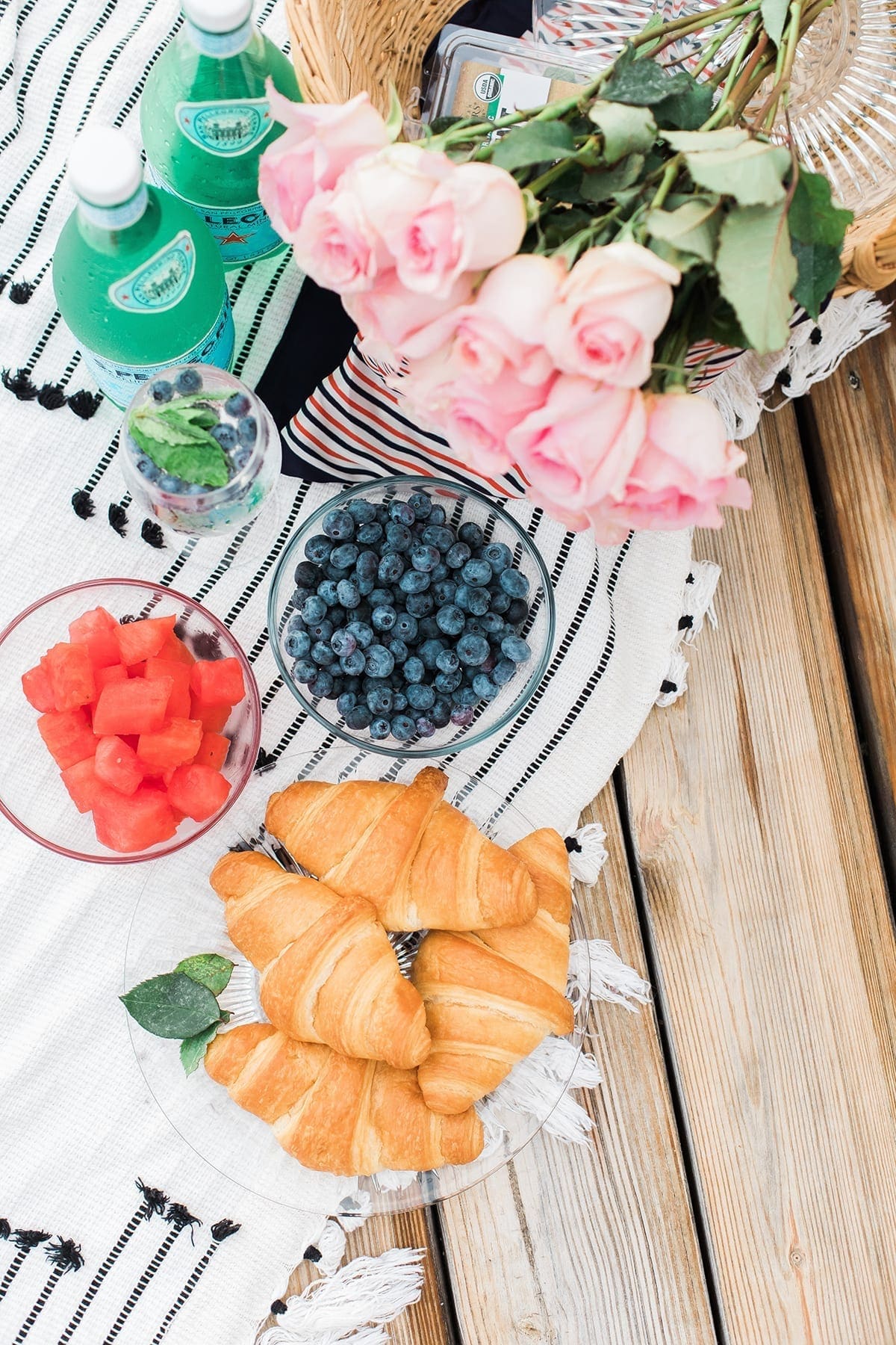 Overhead of a picnic spread with croissants, fruit and roses