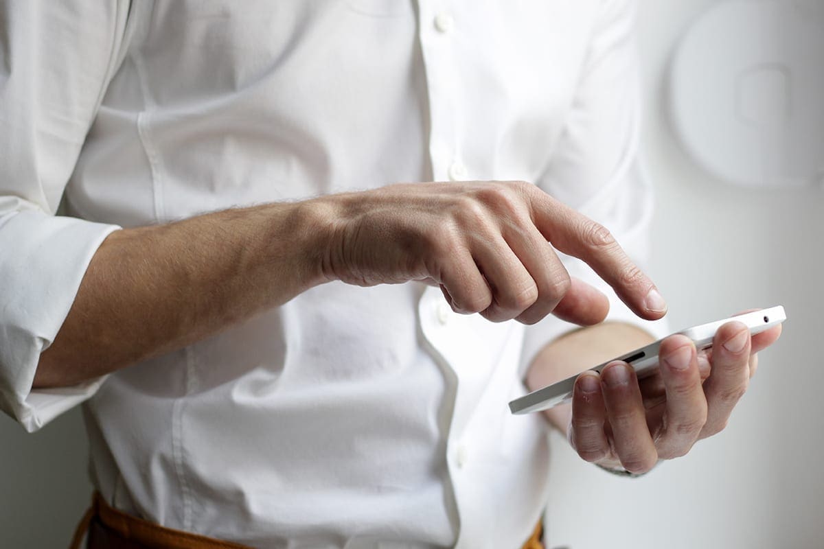 A man in a white shirt types numbers into a cell phone