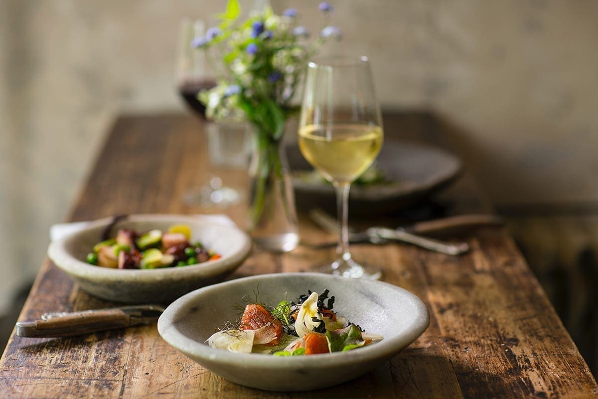 Bowl hold intricate food display and a glass of white wine