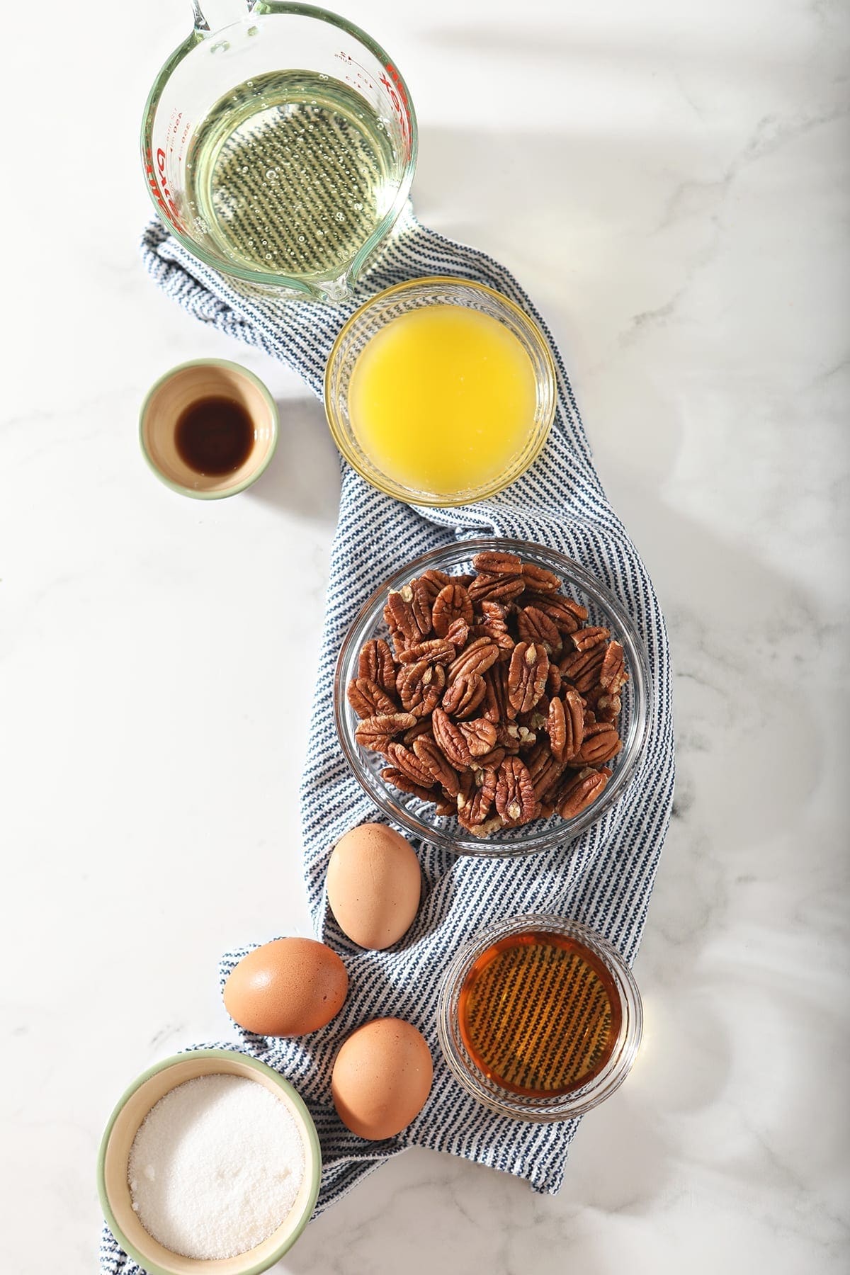 Pecans, butter, eggs, bourbon and other ingredients sit on a blue striped towel before a pie is made