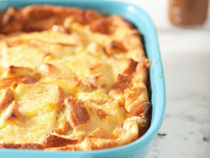 Bread pudding in a turquoise baking dish on a striped towel, after baking
