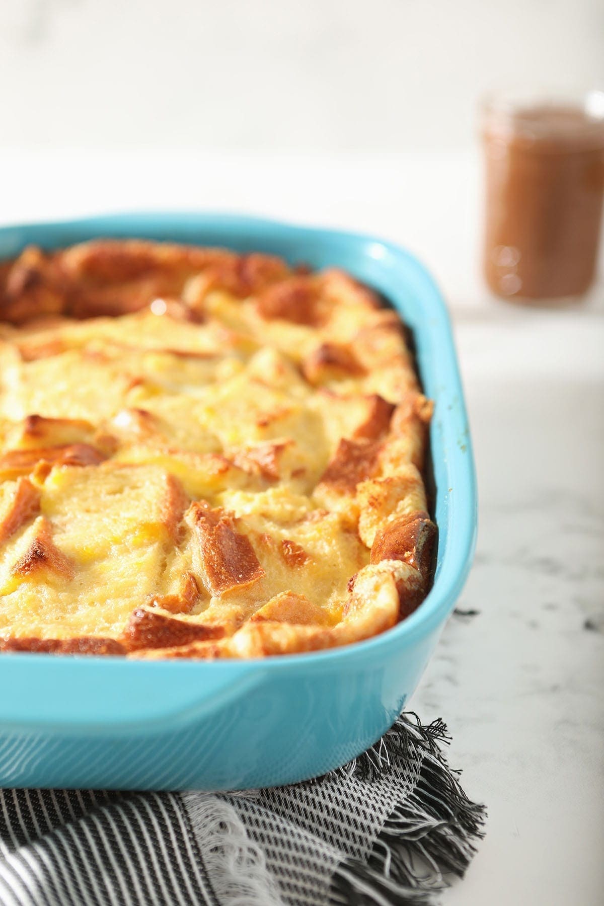 Bread pudding in a turquoise baking dish on a striped towel, after baking