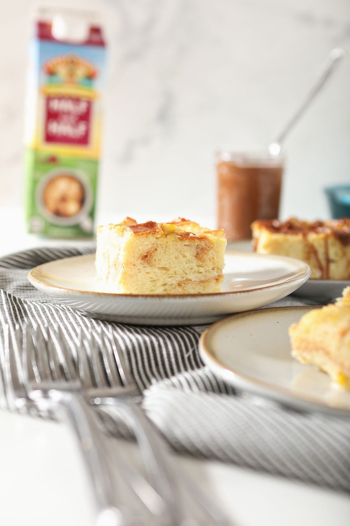 Slices of bread pudding on white pottery plates sitting on a gray towel