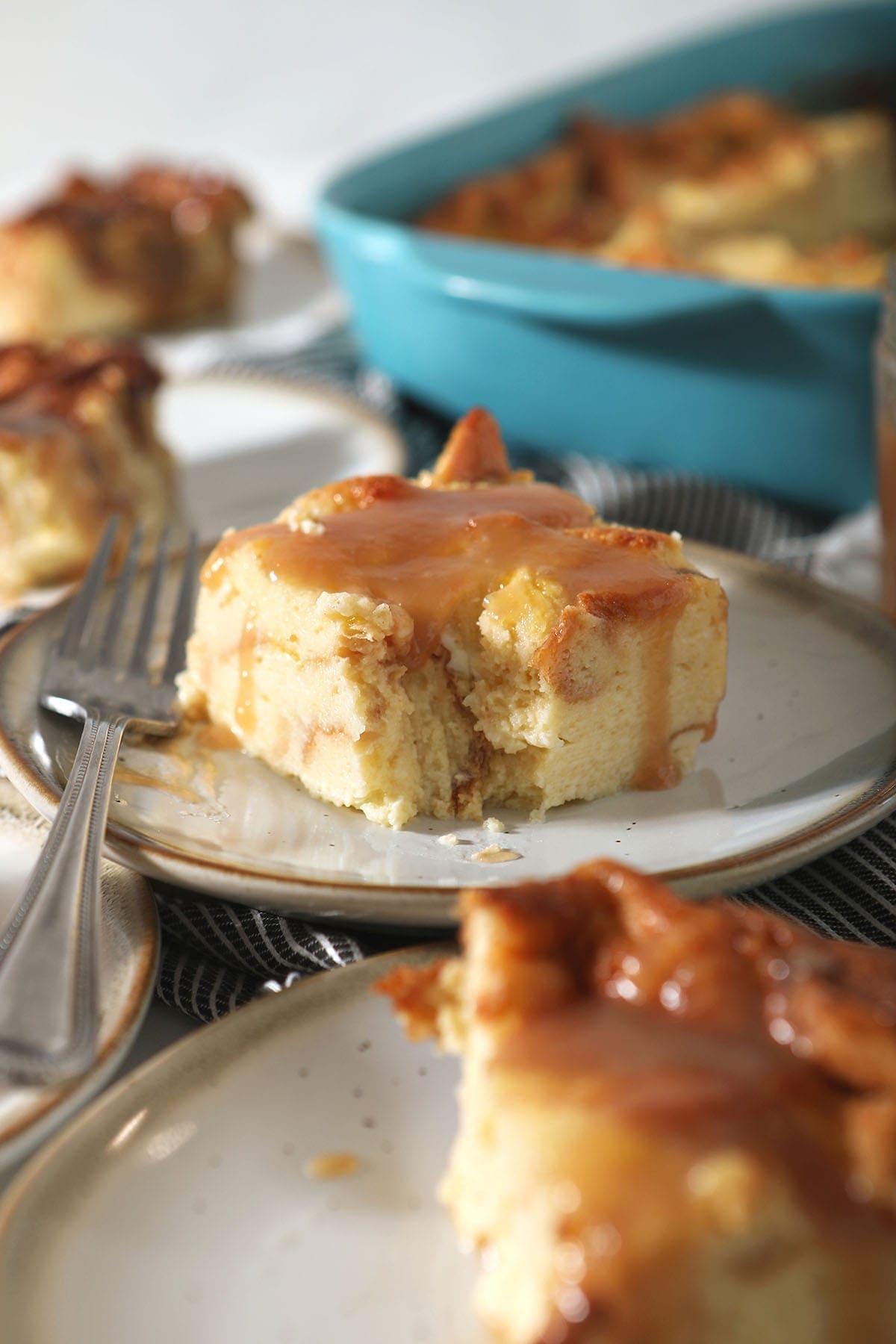 A cut into piece of bread pudding with caramel sauce on a white plate, surrounded by other slices of the dessert