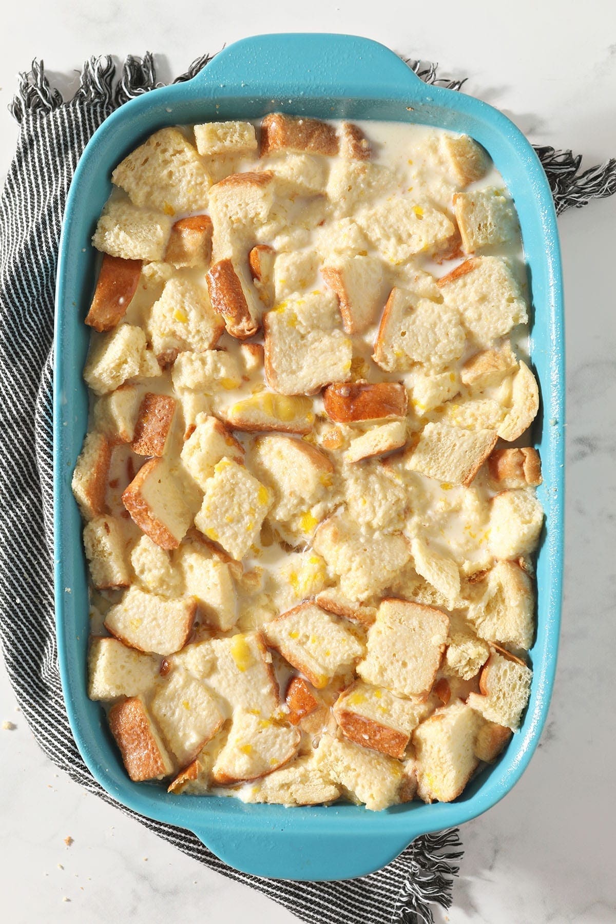 The custard and sliced bread soak together in a turquoise baking dish