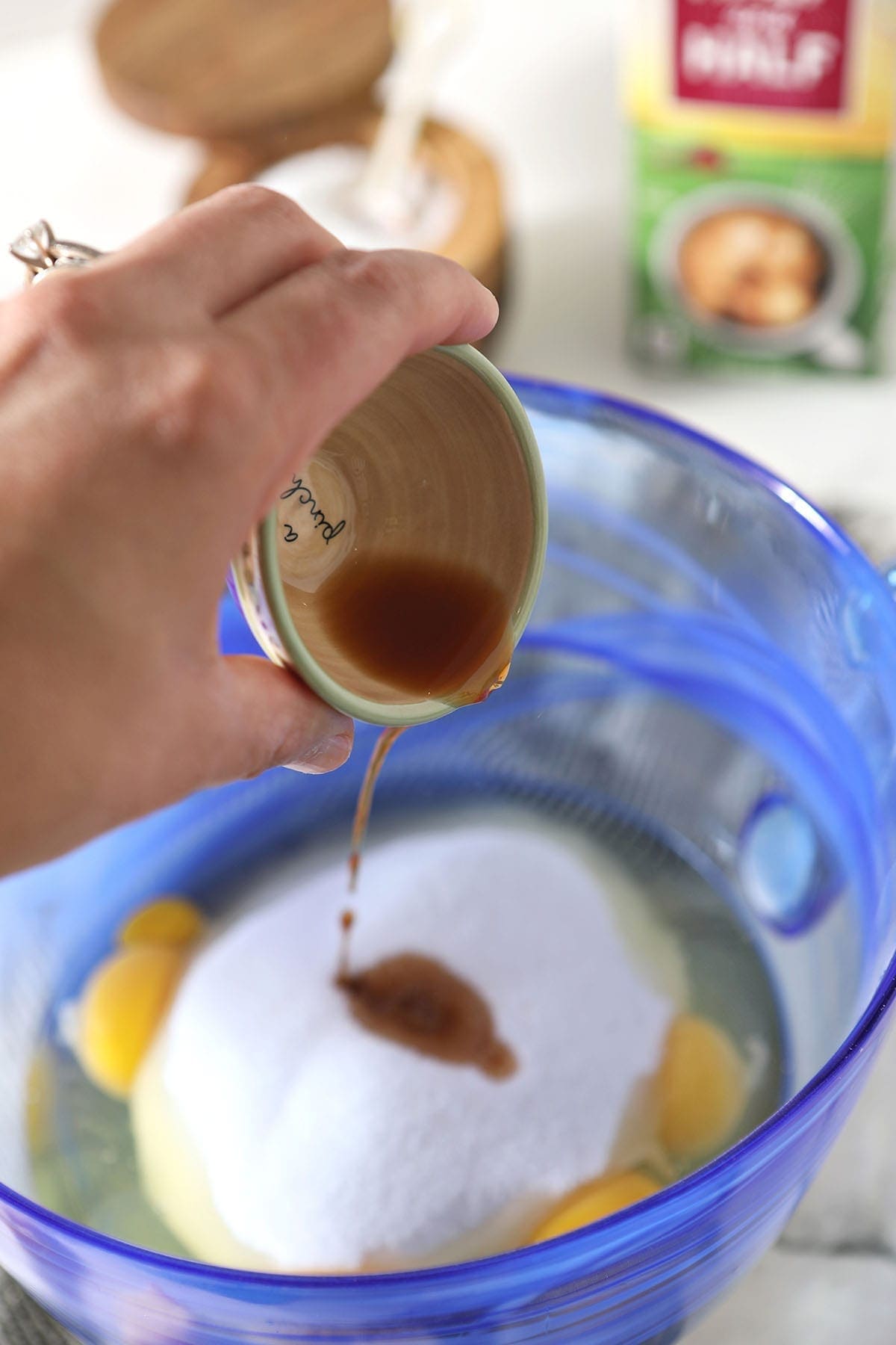 Vanilla pours on top of sugar and eggs in a blue glass bowl