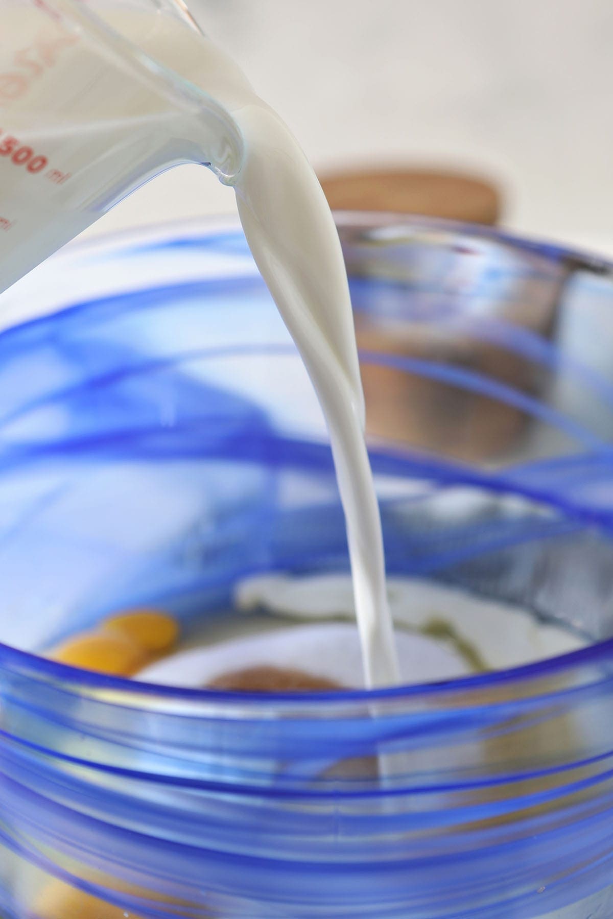 Milk pours into a blue glass bowl holding other ingredients
