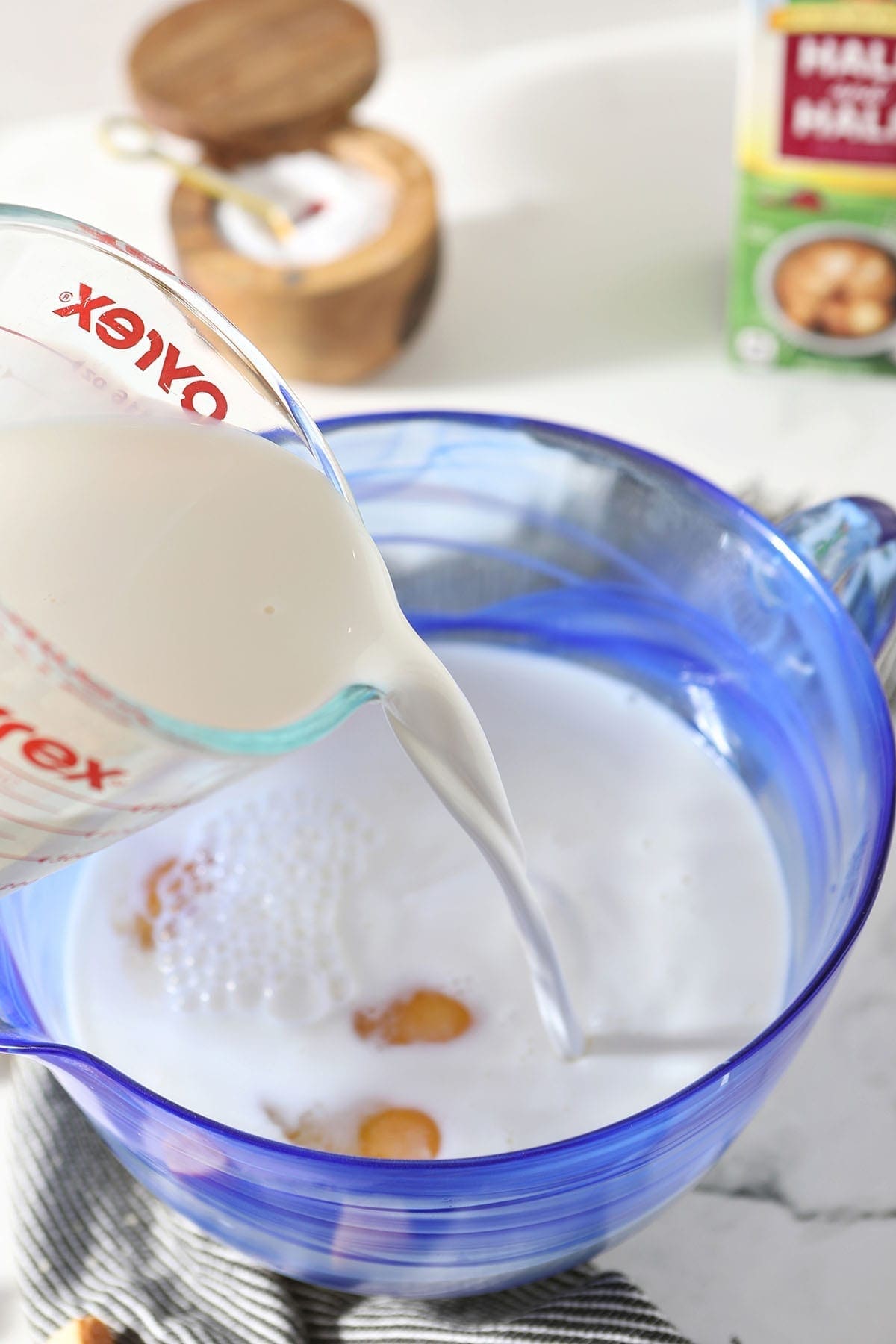 Half & Half pours into a blue glass bowl holding eggs and other ingredients