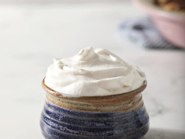 A blue pottery bowl holding a serving of homemade sweetened whipped cream in front of a pink pie plate