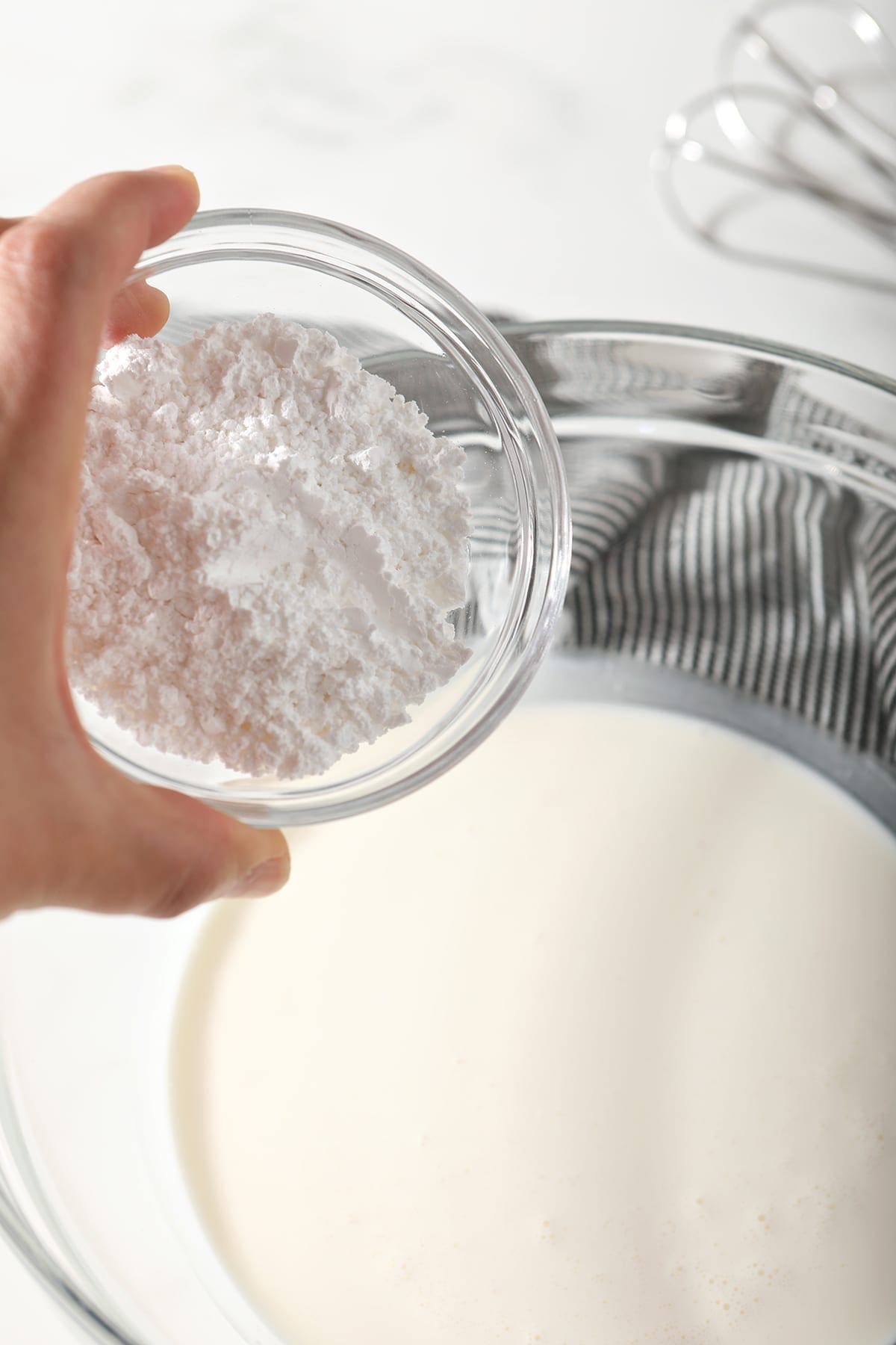 Powdered sugar sprinkles into a bowl of heavy whipping cream