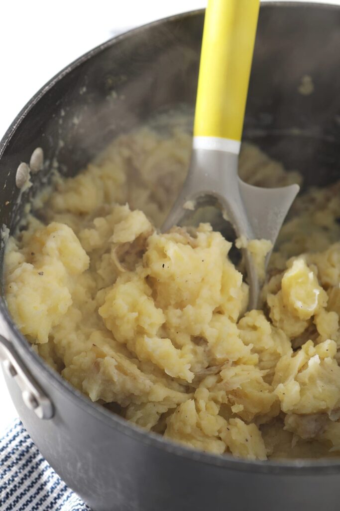 A potato masher is shown in a black pot with mashed potatoes