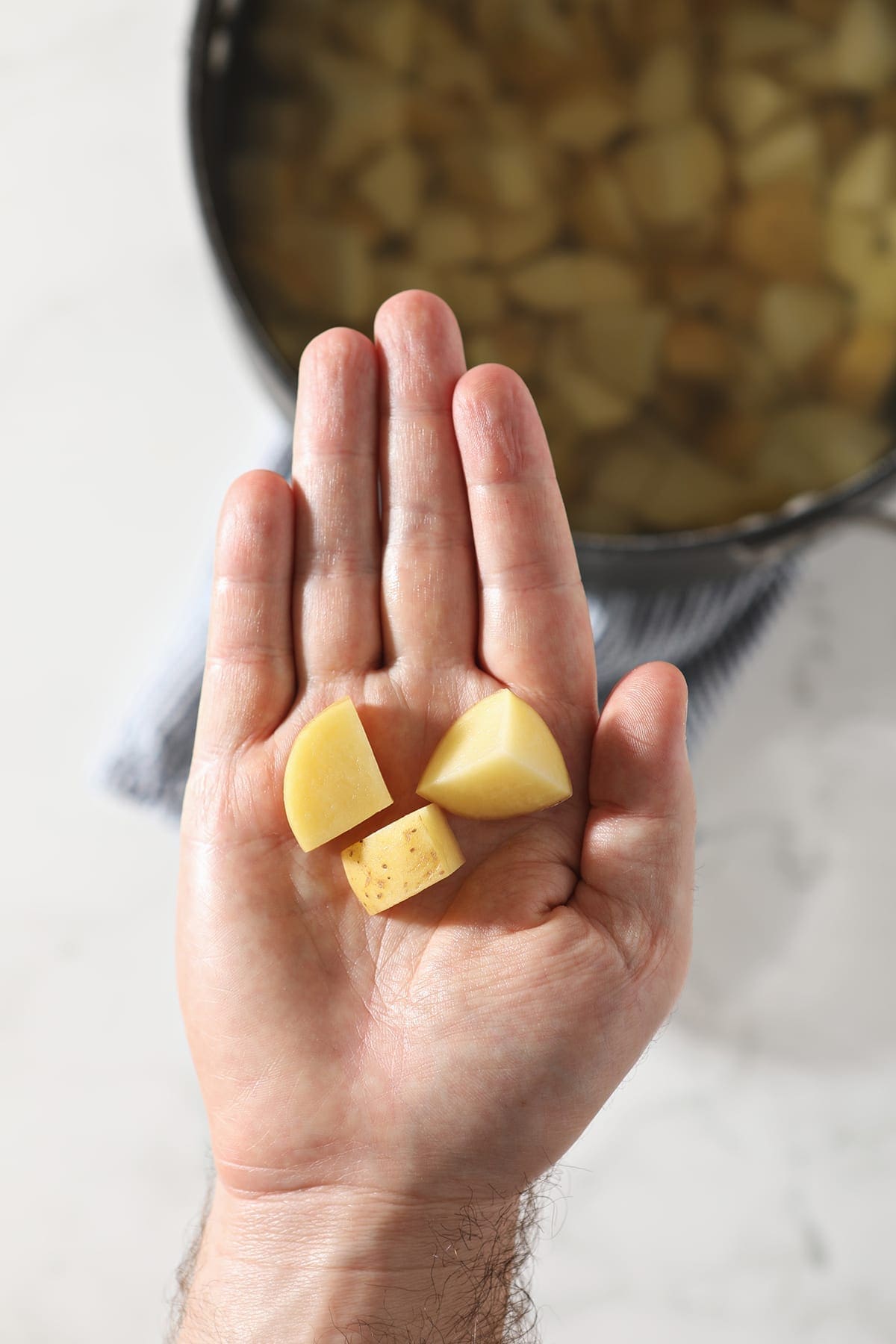 A man holds three potato pieces in his hand above a pot holding more potatoes