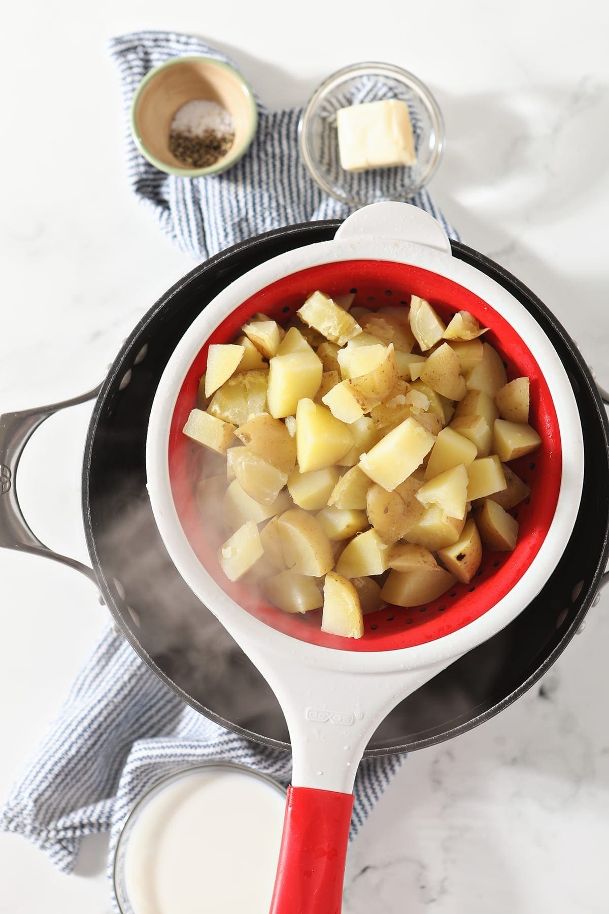 Steam streams off recently boiled potatoes in a red and white colander