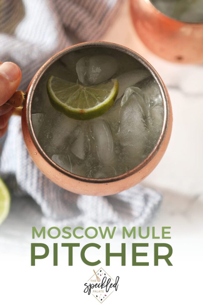 Close up of a Moscow mule inside a copper mug behind held above a blue striped towel with the text 'moscow mule pitcher'