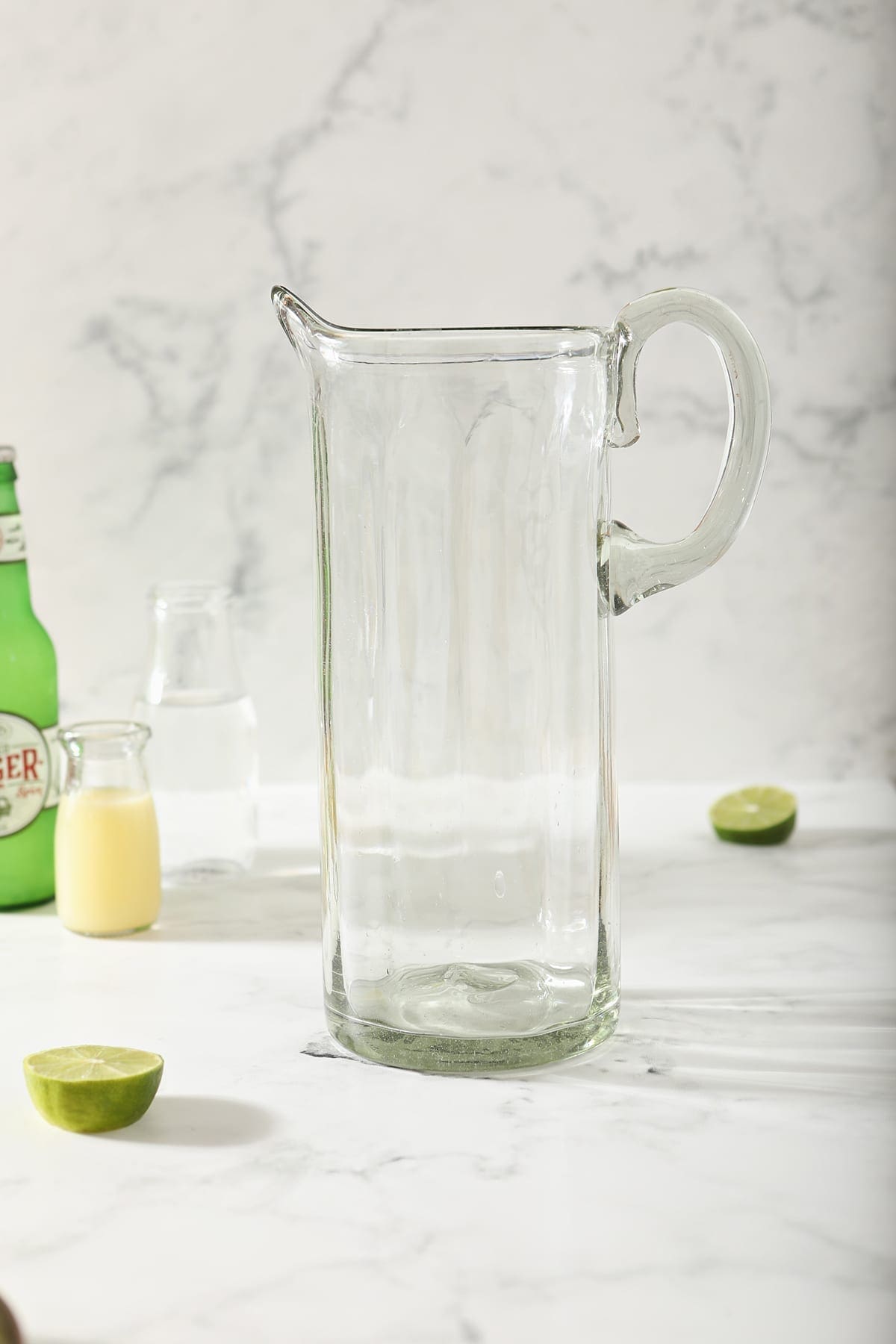 An empty pitcher next to lime juice, vodka and ginger beer