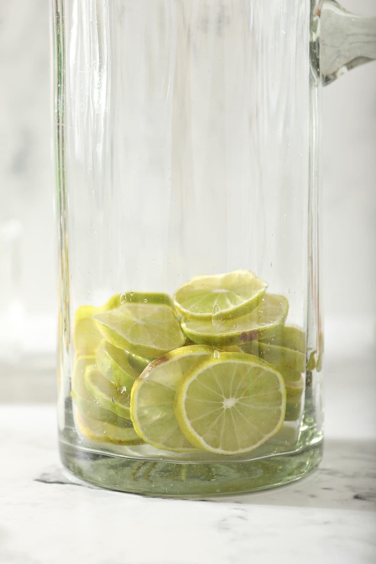 Close up of lime rounds in a tall pitcher sitting on marble