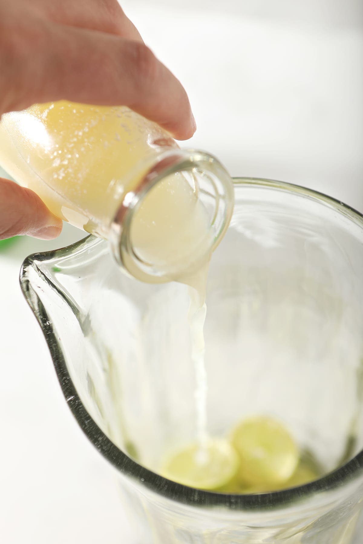 Lime juice pours into a tall pitcher on top of lime rounds