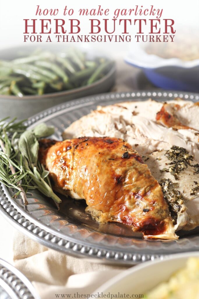 Roasted turkey breast on a silver platter next to fresh herbs with the text 'how to make garlicky herb butter for a thanksgiving turkey'