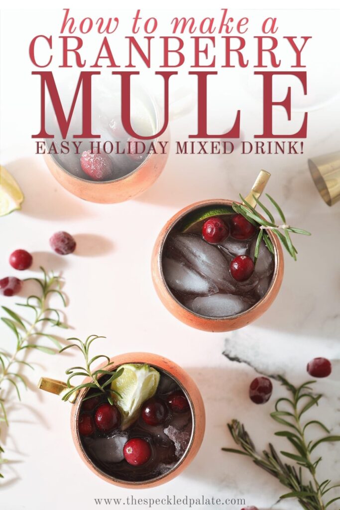 Three Cranberry Mules sit on a marble surface next to a bowl of cranberries, a gold jigger, rosemary sprigs and more cranberries with the text 'how to make a cranberry mule. easy holiday mixed drink!'