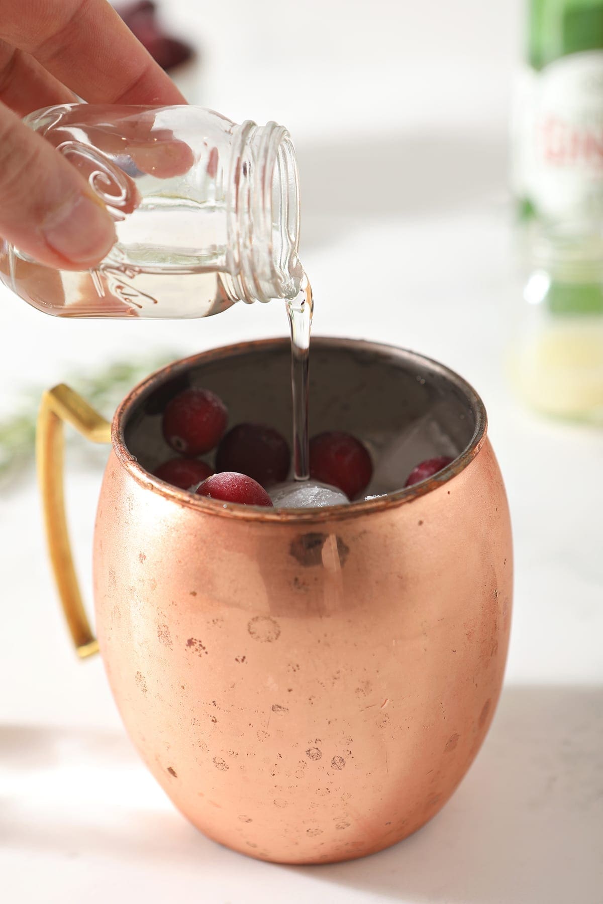 Simple syrup pours into a copper mug holding ice and cranberries