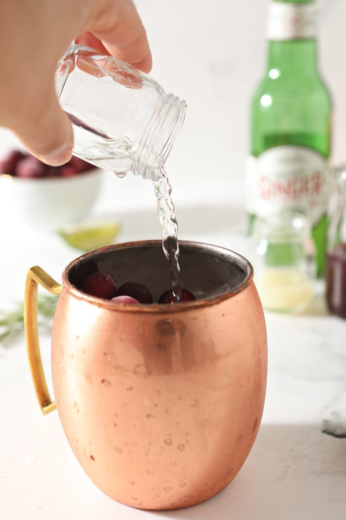 Vodka pours into a copper mug holding ice, syrup and cranberries