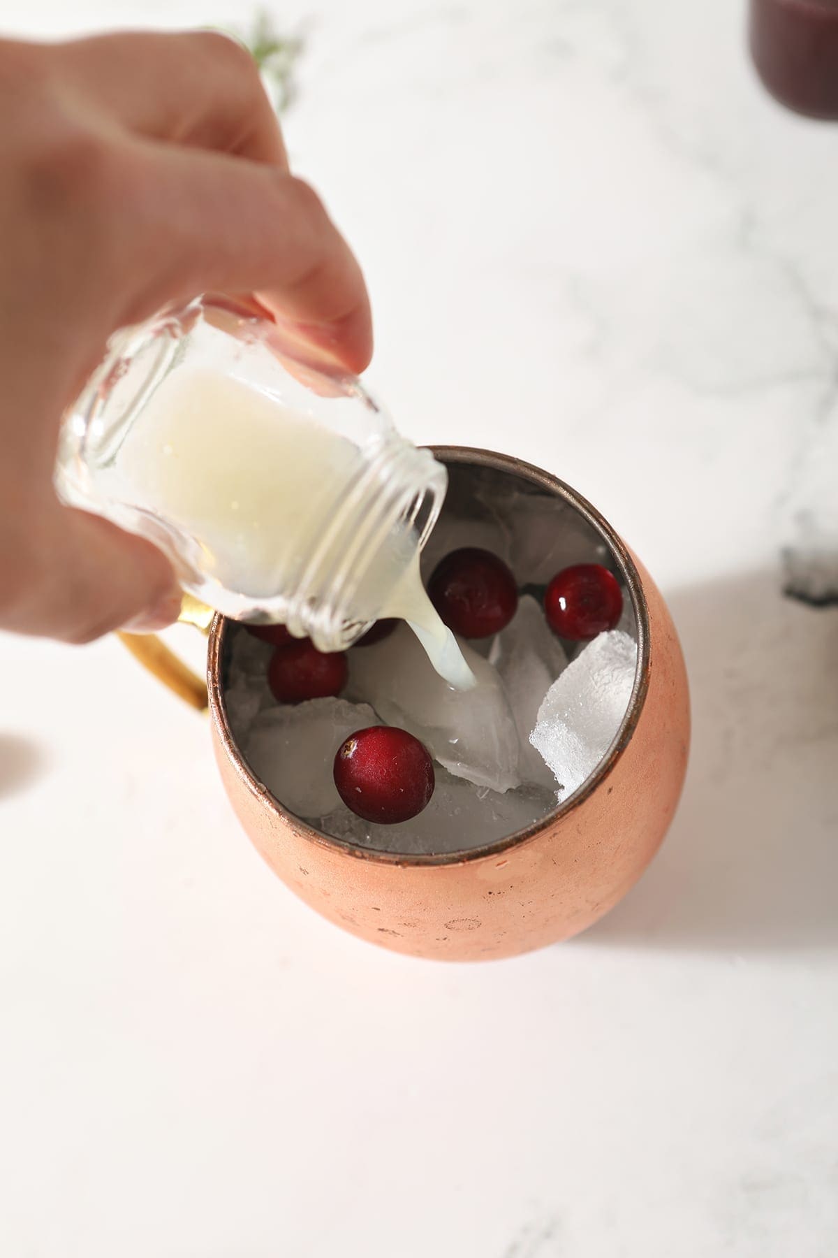 Lime juice pours into a copper mule mug with cranberries and other ingredients