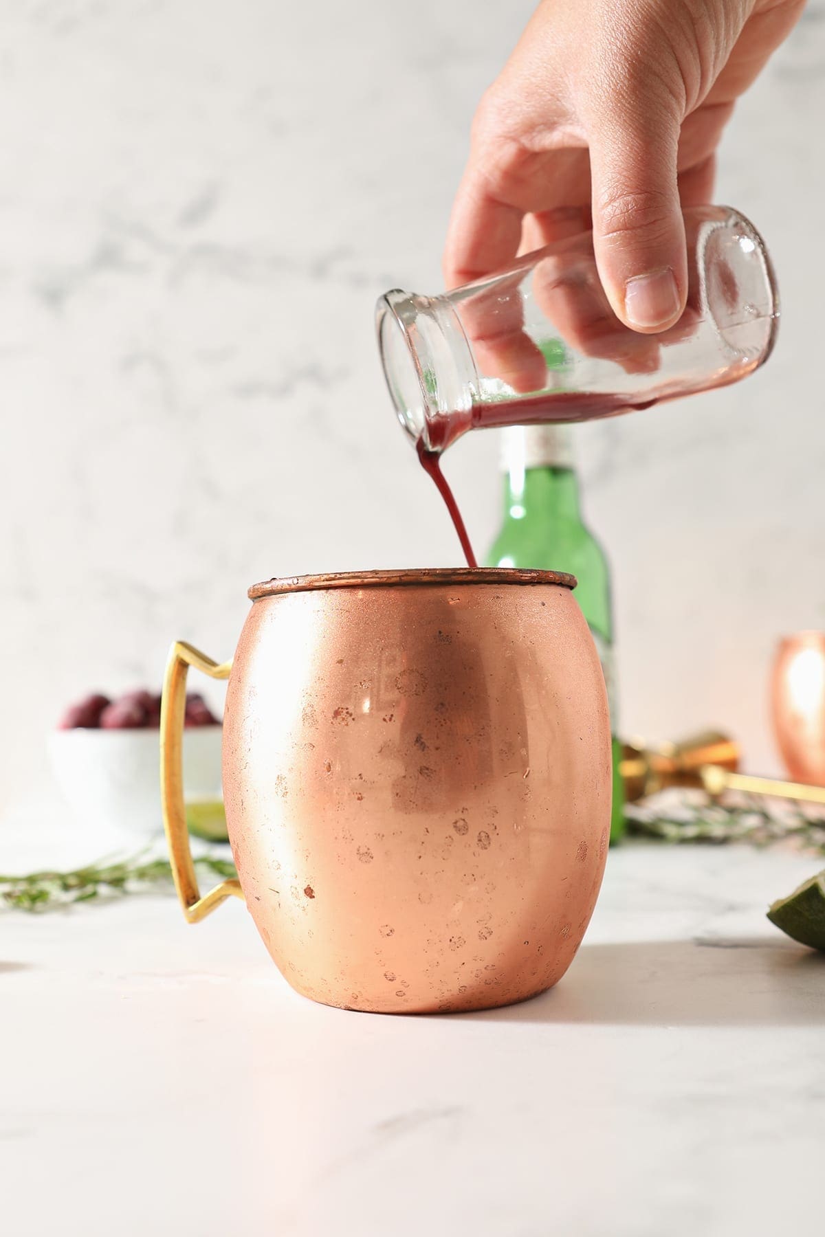 Cranberry juice pours into a copper mug on a marble surface