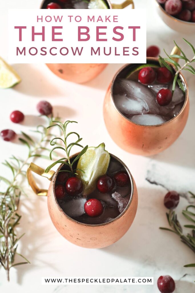 Three Cranberry Mules sit on a marble surface next to a bowl of cranberries, a gold jigger, rosemary sprigs and more cranberries with the text 'how to make the best moscow mules'