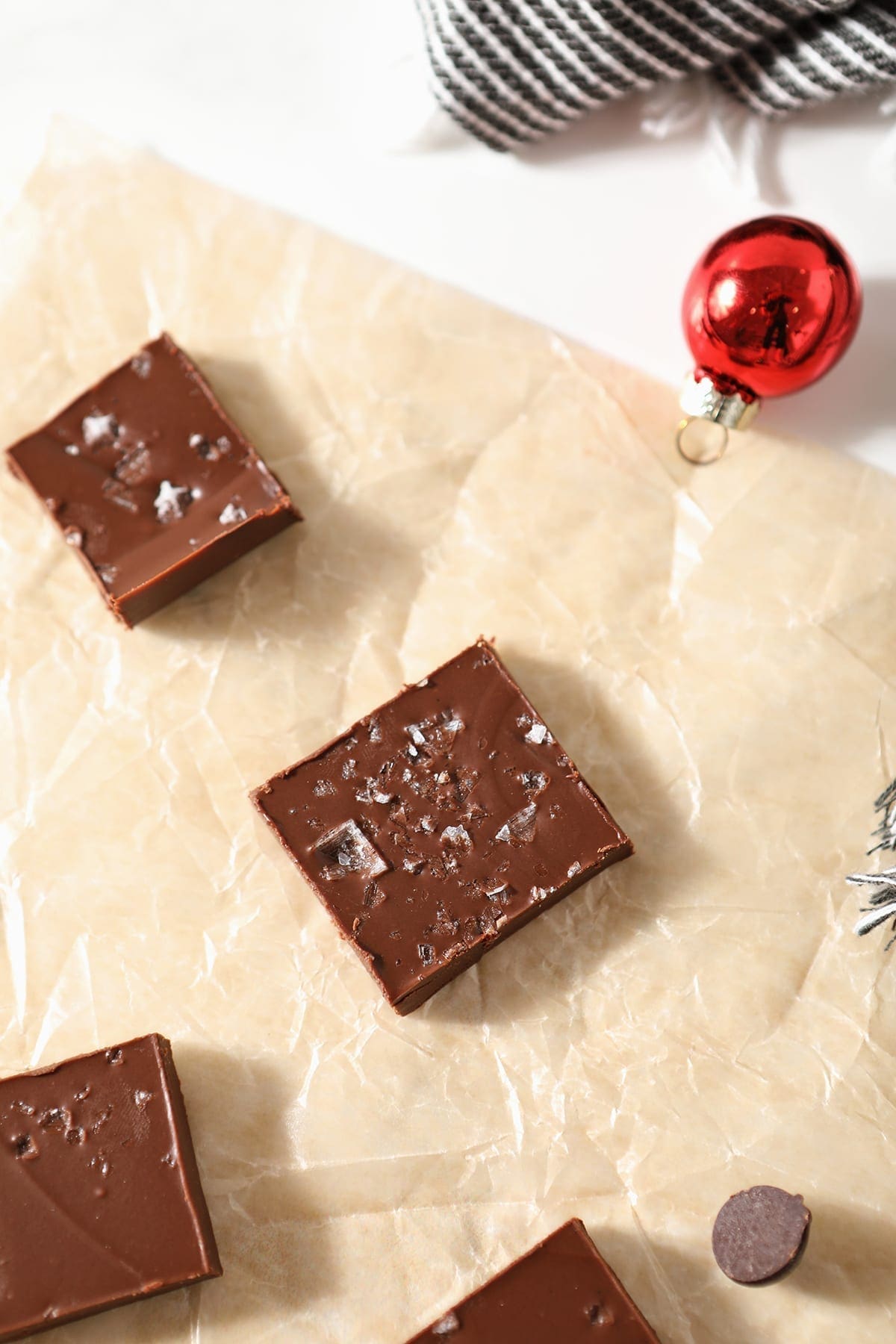 Slices of Peanut Butter Chocolate Fudge on a piece of parchment with a red ornaments and a gray and white towel