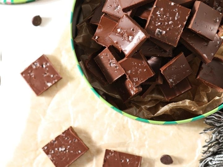Peanut Butter Chocolate Fudge in a festive holiday container next to other slices of fudge on parchment